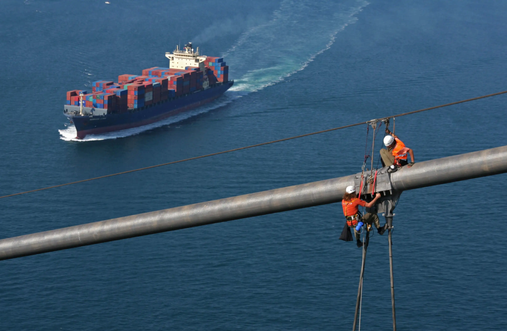 Bridge inspection is one of the steadiest — and most scenic — rope access specializations Rope access technicians working on a bridge cable stay with a container ship passing below